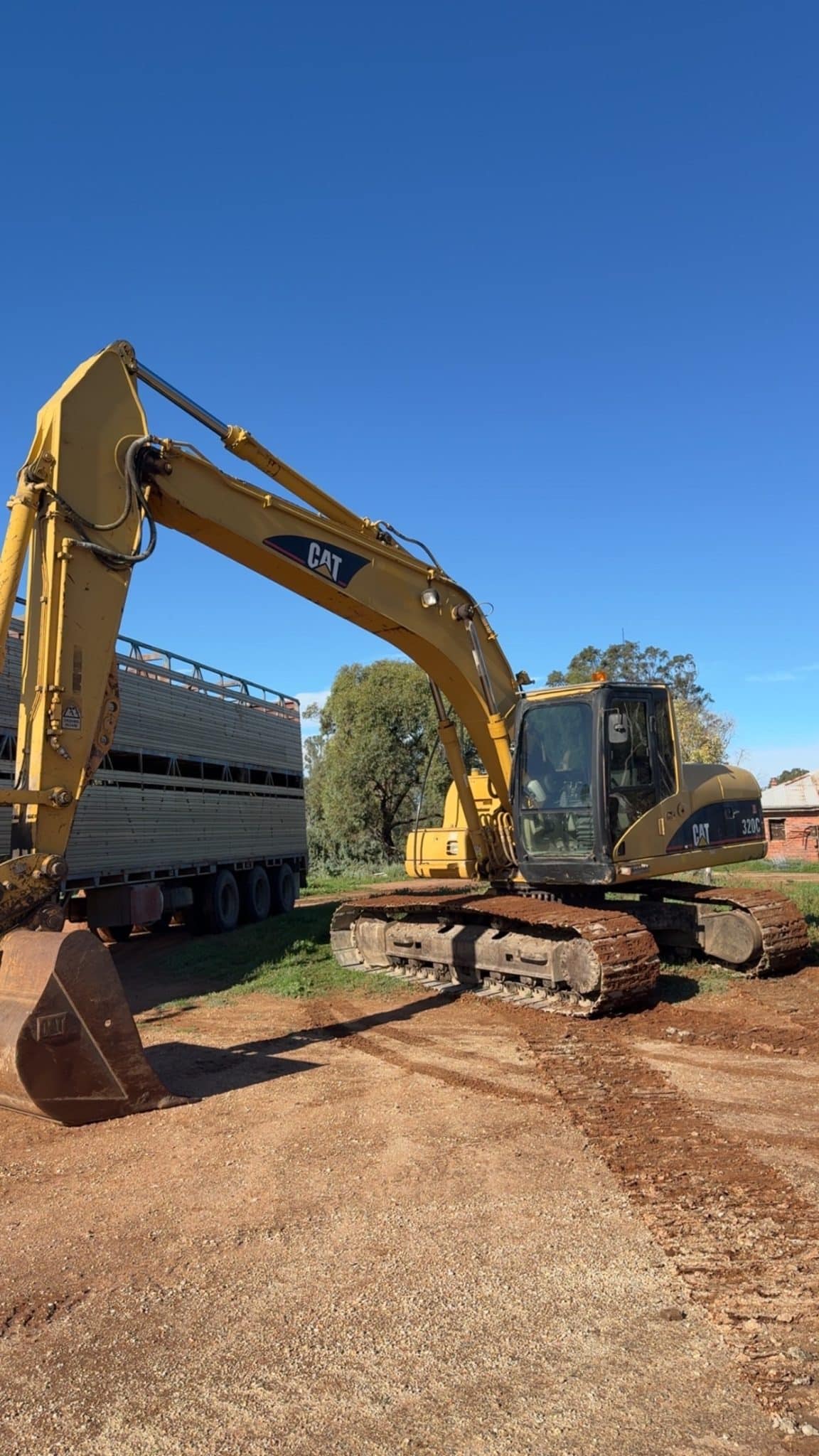Yellow CAT excavator with extended arm and bucket, on a dirt surface under a clear blue sky at a construction site.