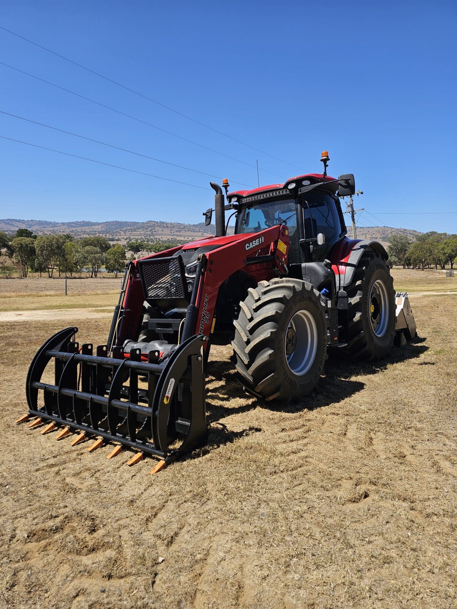 Red Case tractor with front-mounted loader on a dry field under a clear blue sky.