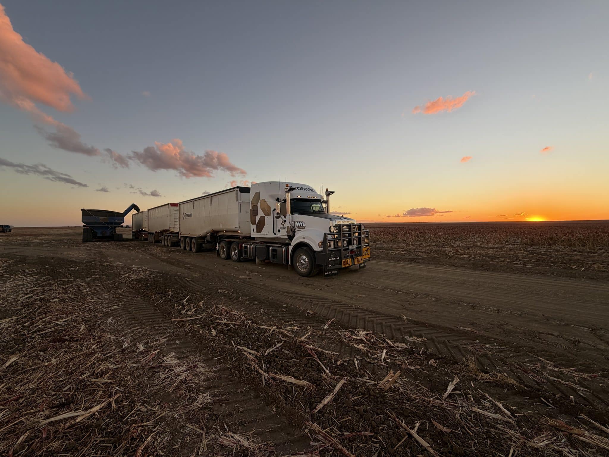 Truck with multiple trailers parked in a harvested field during sunset.