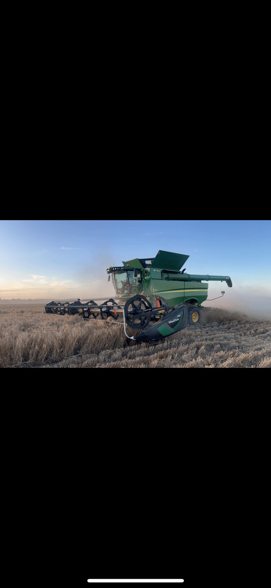 Green combine harvester in a harvested field at sunrise or sunset, ready to harvest with an attached header.
