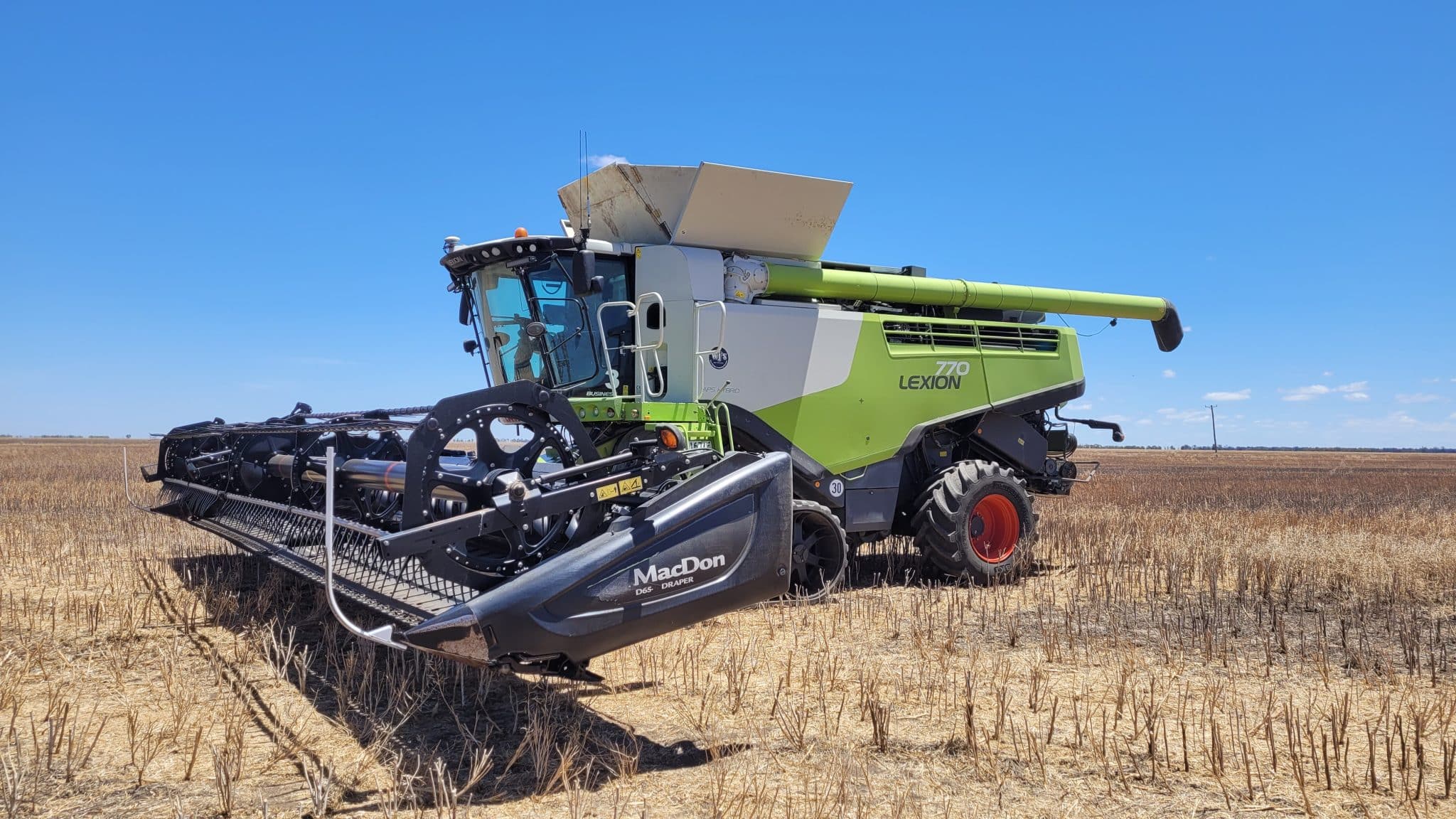 Green CLAAS Lexion 770 combine harvester in a harvested wheat field under a clear blue sky