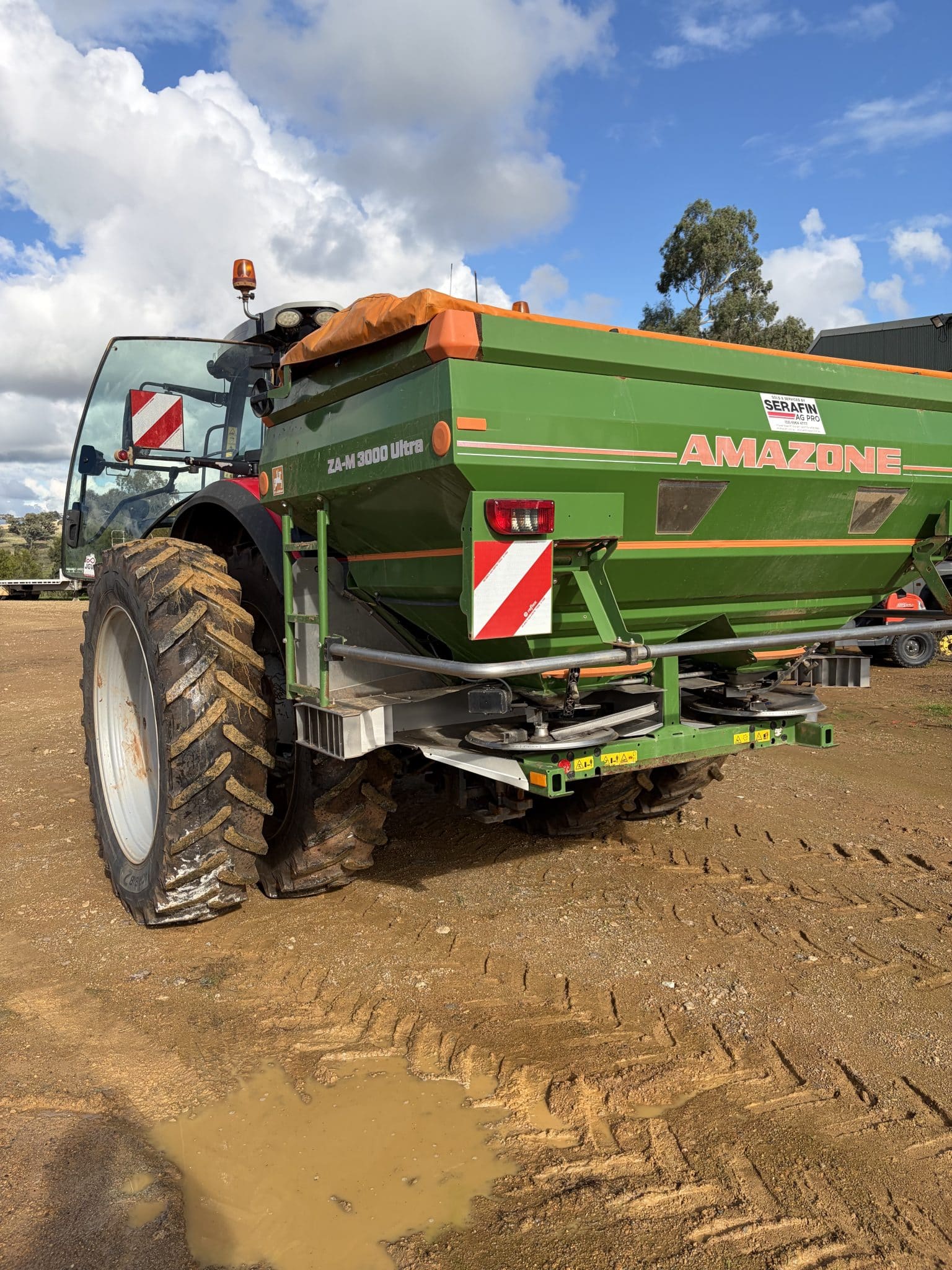 Green AMAZONE ZA-M 3000 Ultra fertilizer spreader on a dirt lot with a muddy puddle in the foreground.